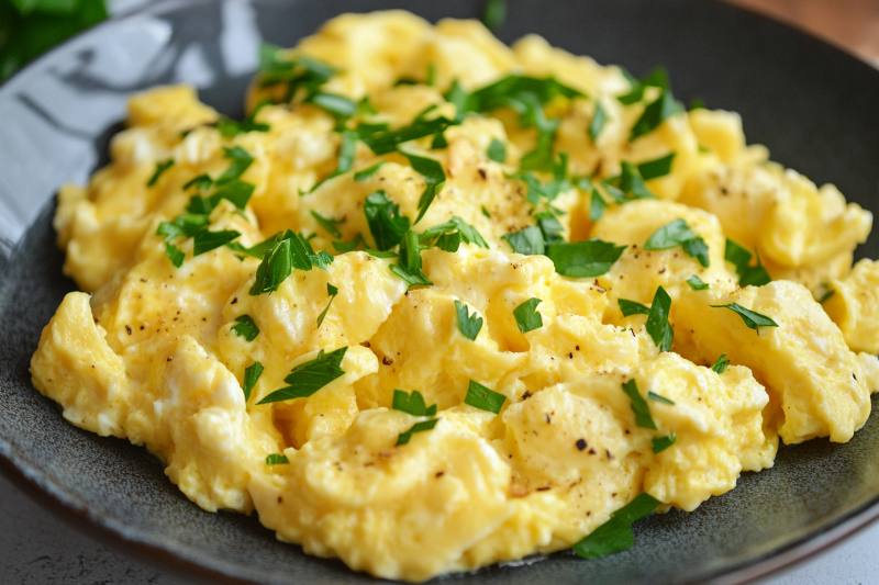 Plate of creamy scrambled eggs garnished with fresh parsley and black pepper