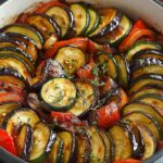 Colorful ratatouille in a round dish, featuring layered slices of zucchini, eggplant, and tomato, garnished with fresh thyme.