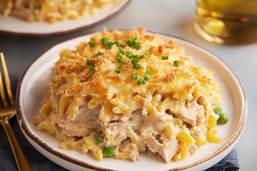 A serving of creamy tuna casserole topped with golden breadcrumbs and garnished with chopped green onions on a white plate.