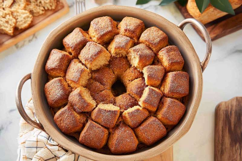 A freshly baked monkey bread in a round baking dish, featuring golden-brown, bite-sized pieces coated with cinnamon sugar.