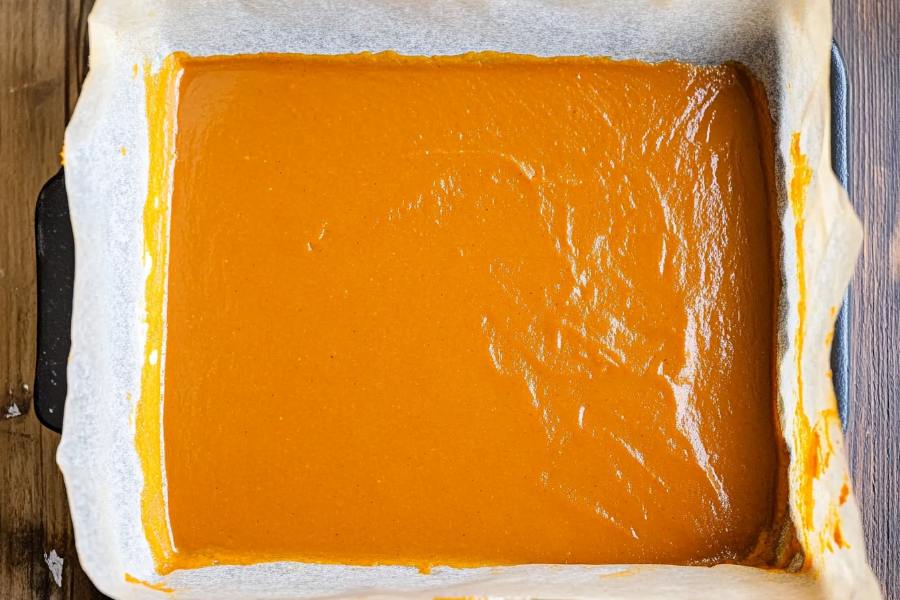 A rectangular baking tray lined with parchment paper filled with a smooth, even layer of pumpkin puree, ready for baking